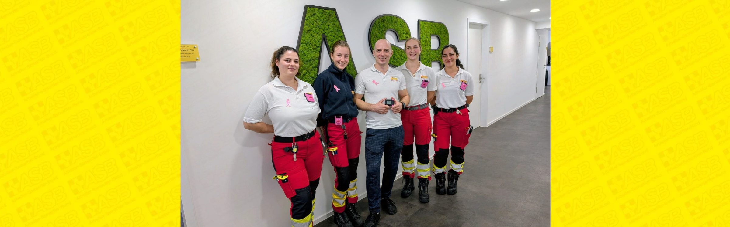 Ein Mann und vier Frauen aus dem Rettungsdienst stehen in einem Gebäude und tragen pinke Funkmeldeempfänger.